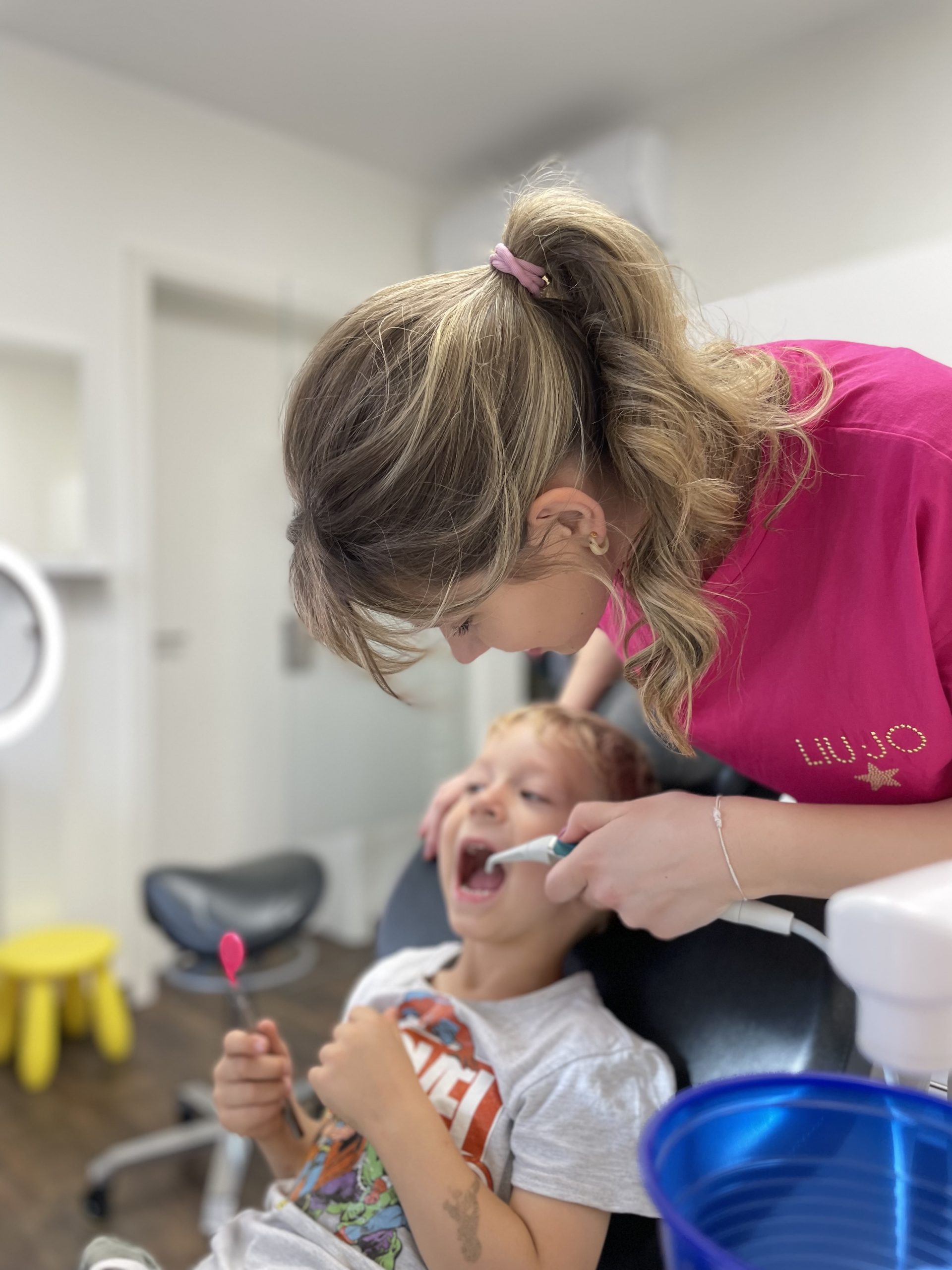 Mitarbeiterin in pinkem Shirt behandelt einen kleinen Jungen in der Kieferorthopädie-Praxis.