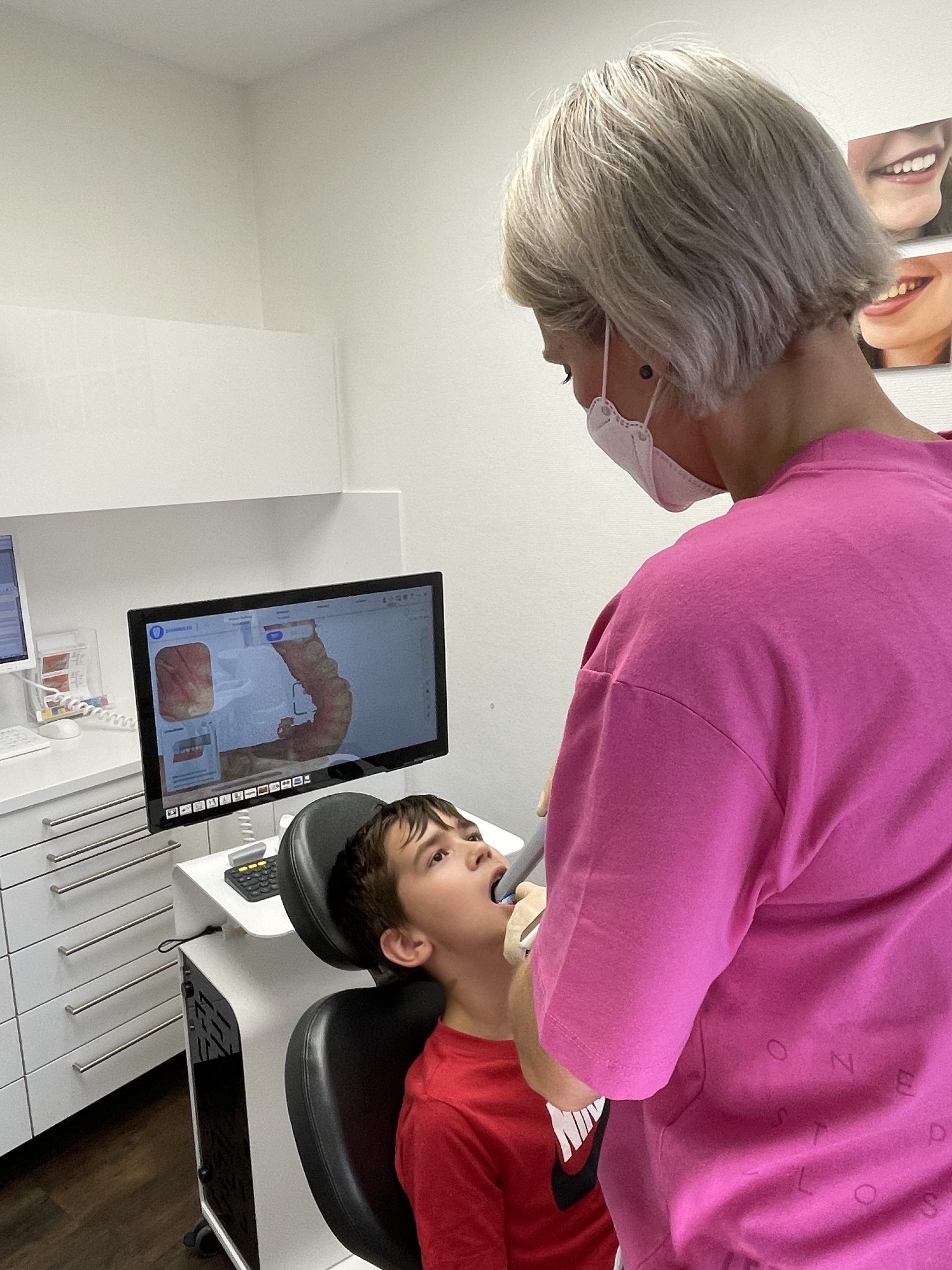 Mitarbeiterin in pinkem Shirt behandelt einen kleinen Jungen in der Kieferorthopädie-Praxis.